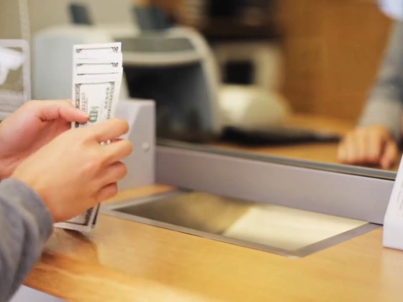 osoba stoji za šalterom u banci i uzima novac