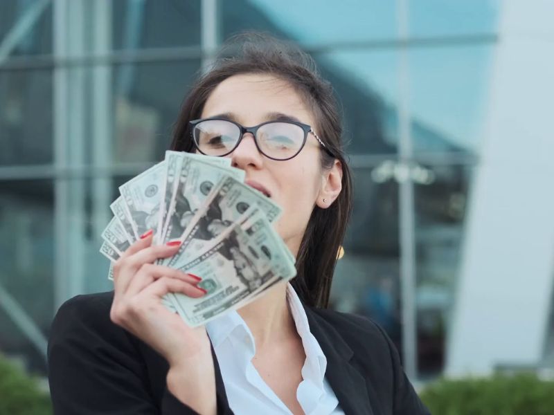 devojka drž i novac u ruci i stoji ispred banke